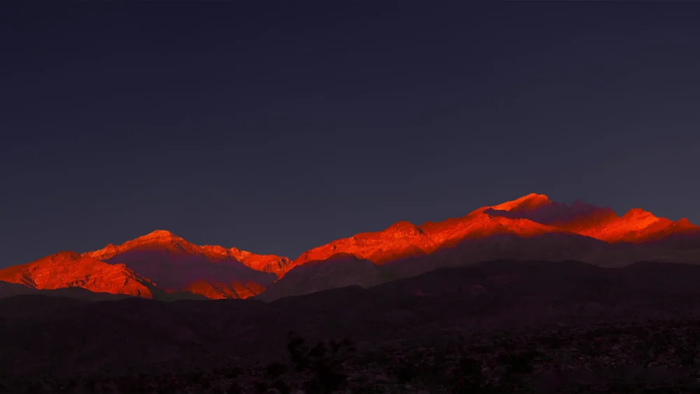 Sierra Nevada peaks lit by alpenglow at sunrise, viewed across the dark floor of Death Valley, California. Panoramic fine art landscape photograph. Large format.
