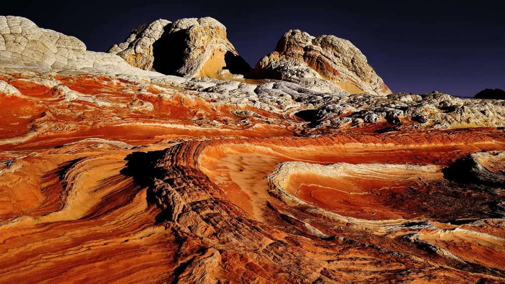 Swirling cross-bedded Navajo sandstone at White Pocket in burning orange, red, and gold under a dark sky, Vermilion Cliffs National Monument, Arizona. Fine art landscape photograph. Fujifilm GFX medium format.
