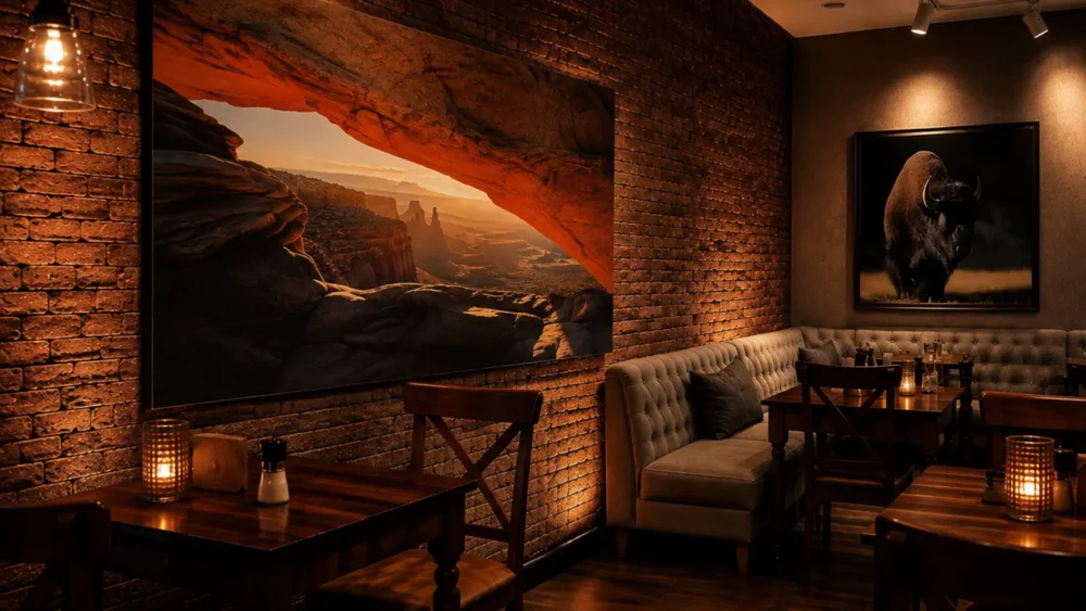 Mesa Arch Sunrise fine art print displayed in an upscale restaurant interior — warm brick wall, ambient lighting, large format landscape photography.