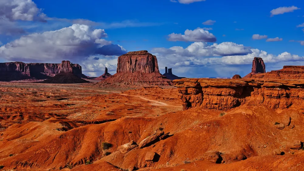 Red sandstone buttes of Monument Valley rise against a vivid blue sky with dramatic cumulus clouds, Navajo Tribal Park, Arizona-Utah border. Fine art landscape photograph. Fujifilm GFX medium format.