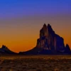 The volcanic neck of Shiprock (Tsé Bitʼaʼí) stands in complete silhouette against a burning twilight gradient sky, deep cobalt transitioning through amber to burning orange at the horizon. Navajo Nation, northwestern New Mexico. Fine art landscape photograph. Nikon medium format