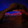 Mobius Arch in the Alabama Hills silhouetted against a starry night sky, framing the distant Sierra Nevada peaks illuminated in pink alpenglow at first light. Alabama Hills, Inyo County, California. Fine art landscape photograph with astrophotography composition. Nikon medium format