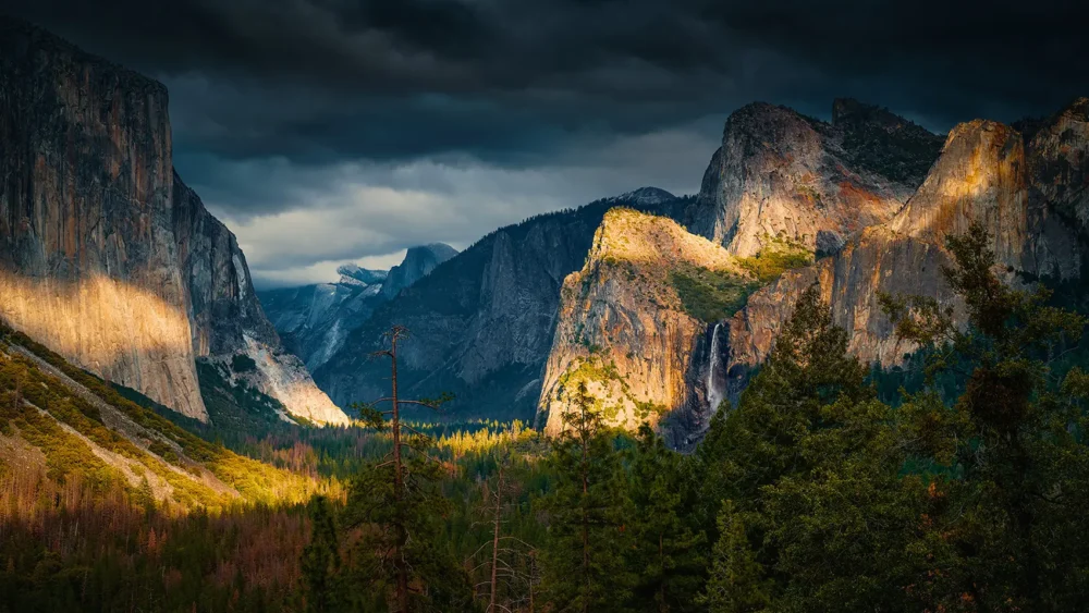 A winter storm breaks over Yosemite Valley — El Capitan lit in afternoon sun, storm clouds above, Bridalveil Fall visible at right. Tunnel View, February 2018. Nikon D810. Fine art photograph