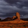 Red sandstone buttes of Monument Valley illuminated by a break in dark storm clouds while the surrounding desert remains in shadow, Navajo Tribal Park, Arizona-Utah border. Fine art landscape photograph. Fujifilm GFX medium format.