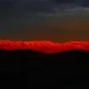 The Panamint Range ignites in deep crimson alpenglow at sunset, viewed across the dark floor of Death Valley, California. Panoramic fine art landscape photograph. Hasselblad X1D II medium format.