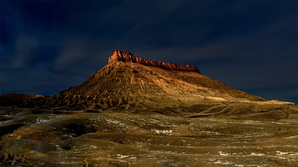 An isolated sandstone ridge lit by the last warm light of day against a deep blue dusk sky, Badlands, Utah. Fine art landscape photograph, large format