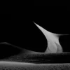 A single curved dune ridge lit by sidelight against pure black shadow at Eureka Dunes, Death Valley National Park, California. Black and white fine art landscape photograph. Fujifilm GFX