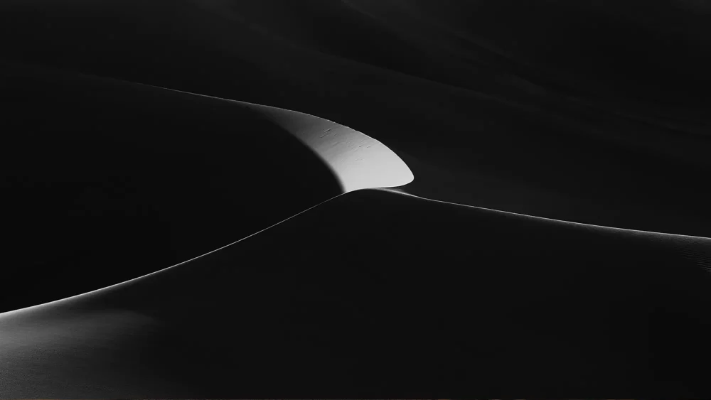 A single arc of white dune sand curves against pure black shadow at Eureka Dunes, Death Valley National Park. Square-format black and white fine art photograph. Fujifilm GFX medium format