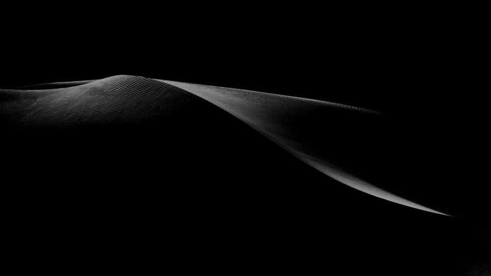 A single silver-lit dune ridge extends across pure black shadow at Eureka Dunes, Death Valley National Park. Signature Series panoramic black-field fine art photograph. Phase One medium format